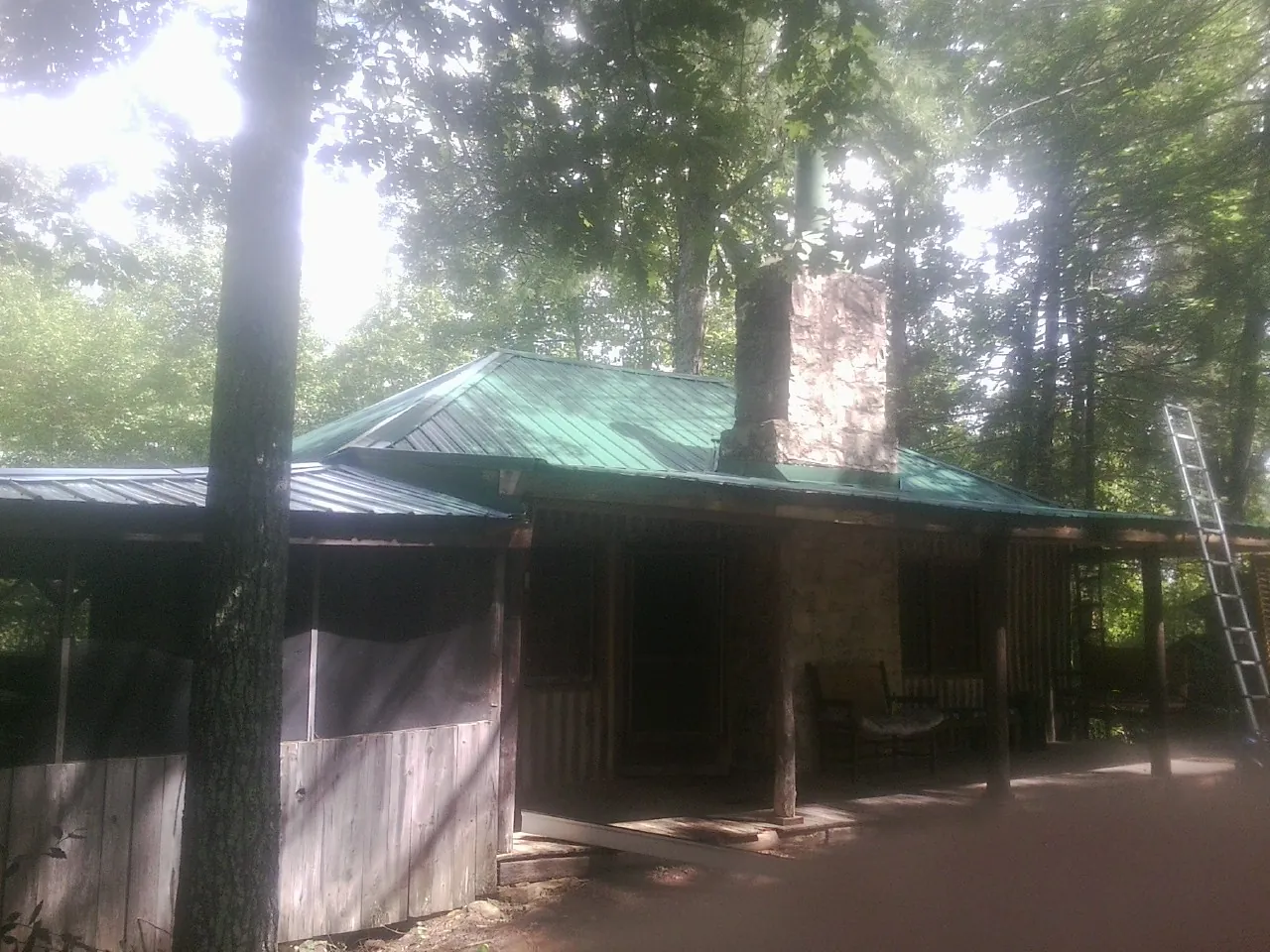 Green metal roof and stone chimney above a log cabin porch in Dublin